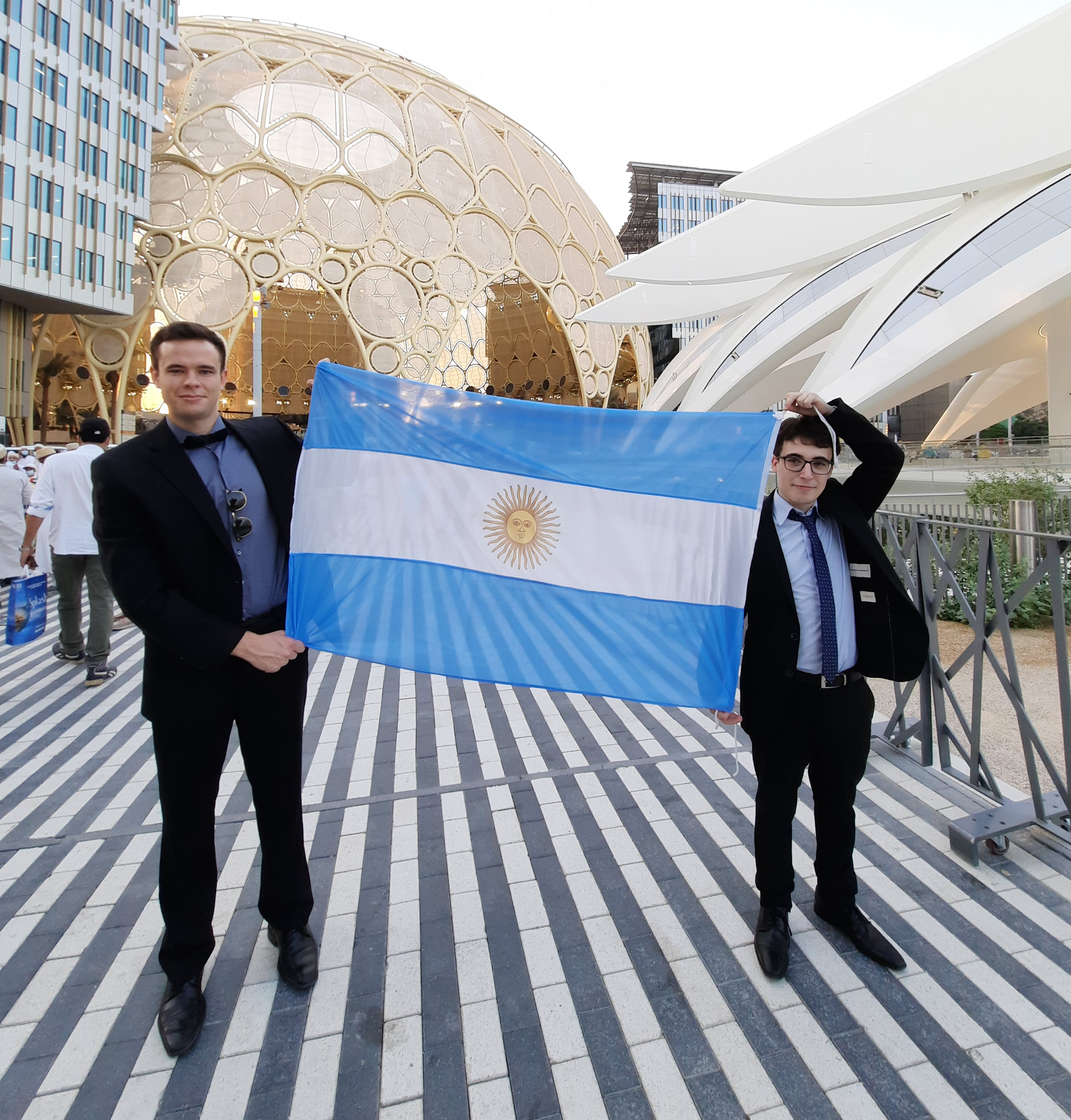 Con la bandera argentina, Tomás Boschetto y Franco Ruffini. En el fondo un domo que es característico de la Expo.